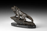 Angled view of majestic bronze lion statue walking across a rugged rock formation