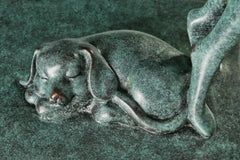 Close-up of the sleeping bronze dog beside the woman's feet with green patina and bronze highlights