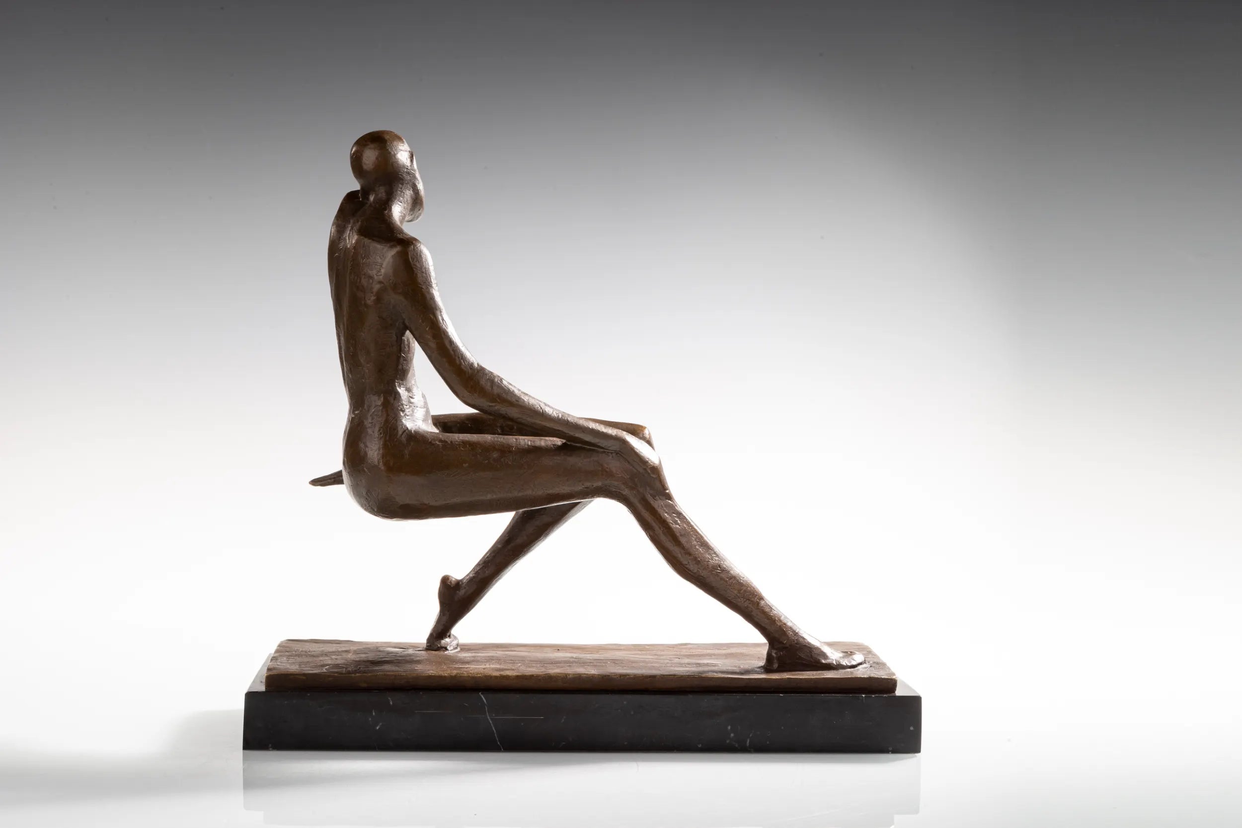 Side angled view of seated female bronze sculpture with long extended legs