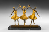 Front view of three ballerinas bronze sculpture with joined hands and golden dresses